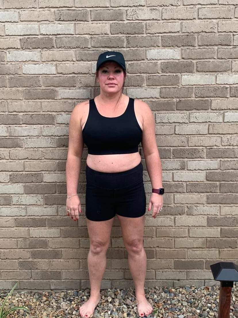 Female client before photo, standing against a brick wall in black training top and shorts