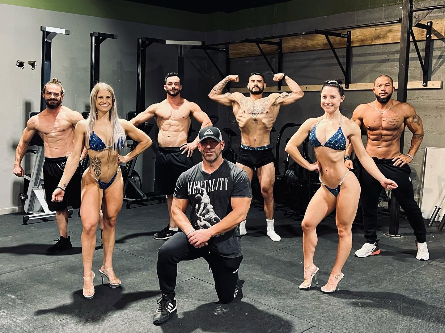 Brink Physiques competition team of male and female physique athletes posing with their coach inside the gym during contest prep