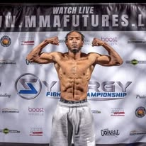 Brink Physiques athlete flexing in contest condition in front of an event banner