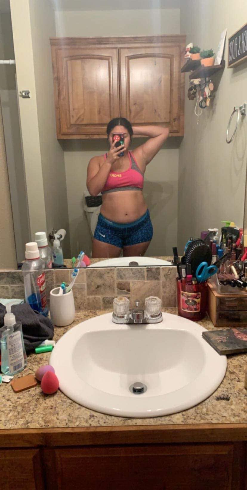 Before photo of a female client at her starting point, mirror selfie in workout clothes