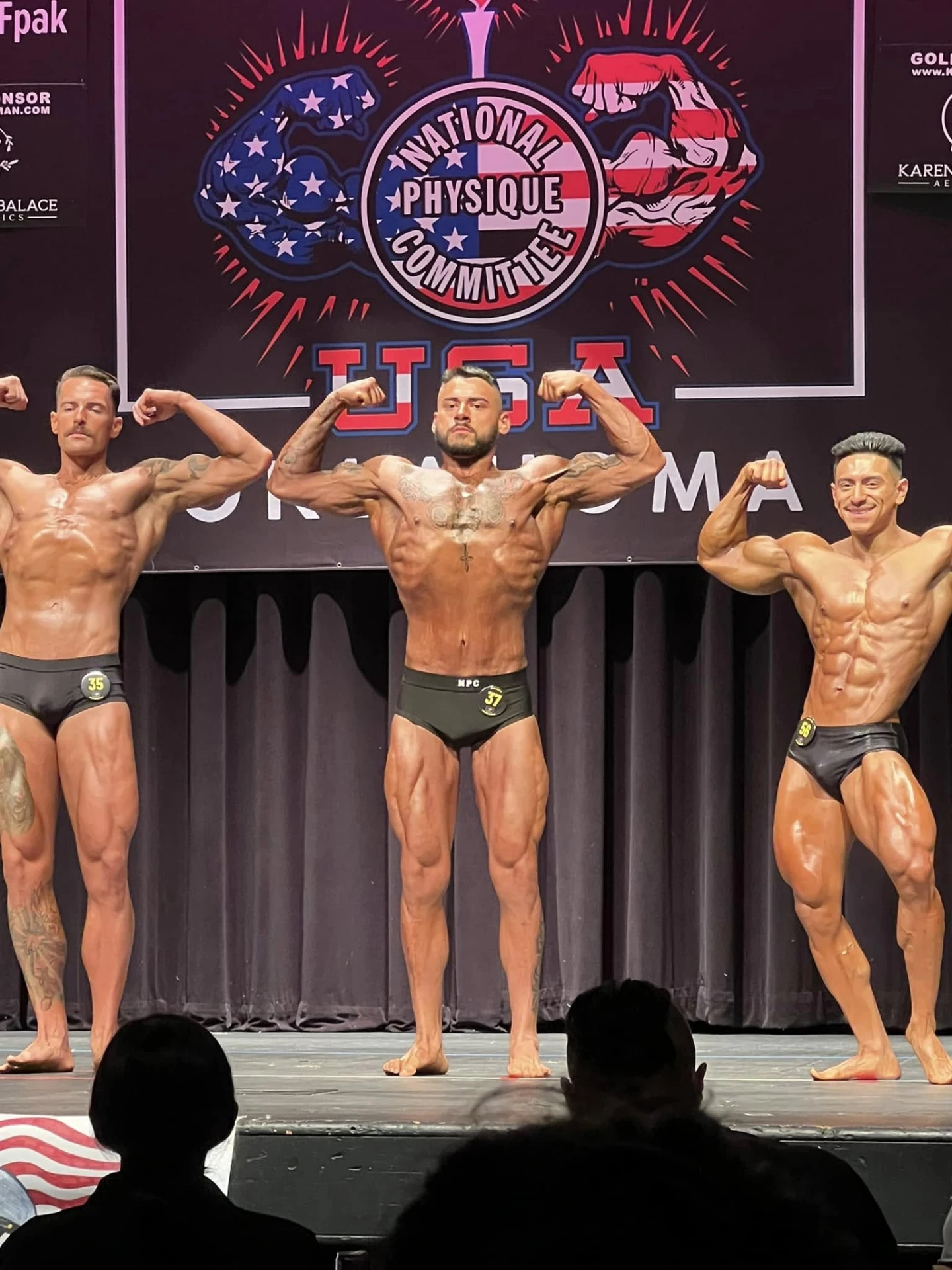 Competitors compared side by side in a front double biceps pose on an NPC Oklahoma stage