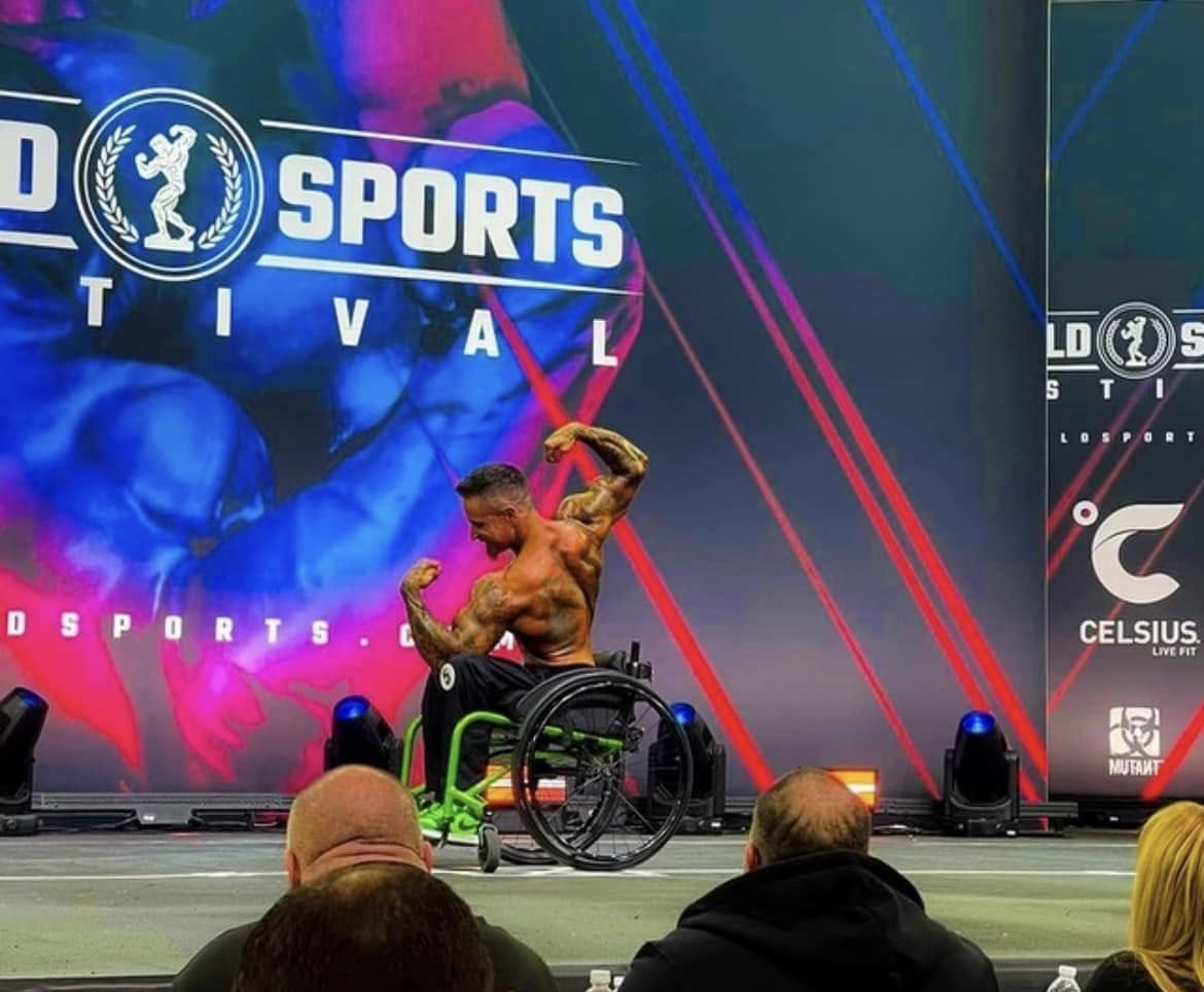 Brink Physiques competitor posing on a major bodybuilding stage while using a wheelchair