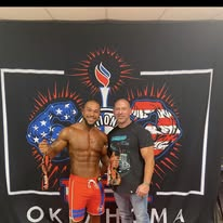 Brink Physiques competitor holding trophies alongside coach Josh after an Oklahoma show