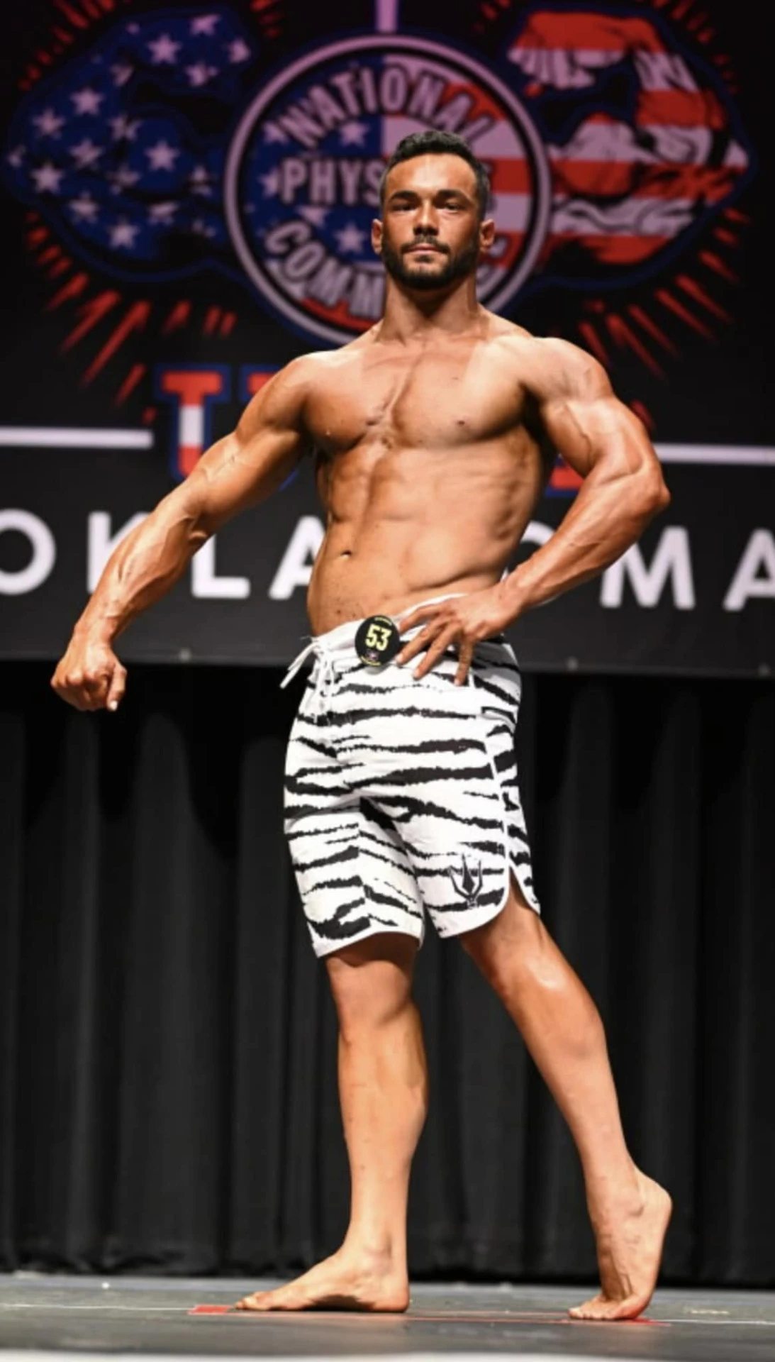 Brink Physiques athlete posing on stage in men's physique competition shorts