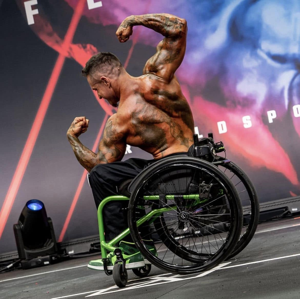 Brink Physiques wheelchair competitor hitting a back pose under the lights on a major stage