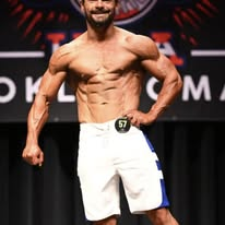 Men's physique athlete posing on stage in contest conditioning